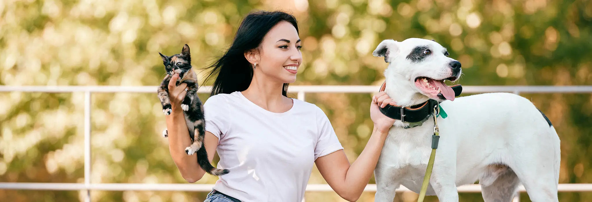 Woman holding a cat and a dog outdoors with a blurred background